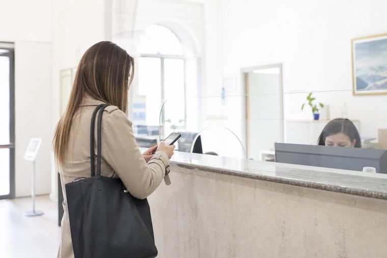 Una persona seduta su un muretto davanti a un edificio pubblico con facciata vetrata.